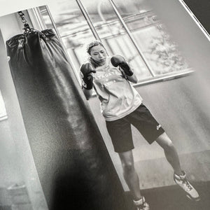 Black and white photograph of a woman professional boxer warming up for a heavy bag session in Shinsei Boxing Gym Japan.